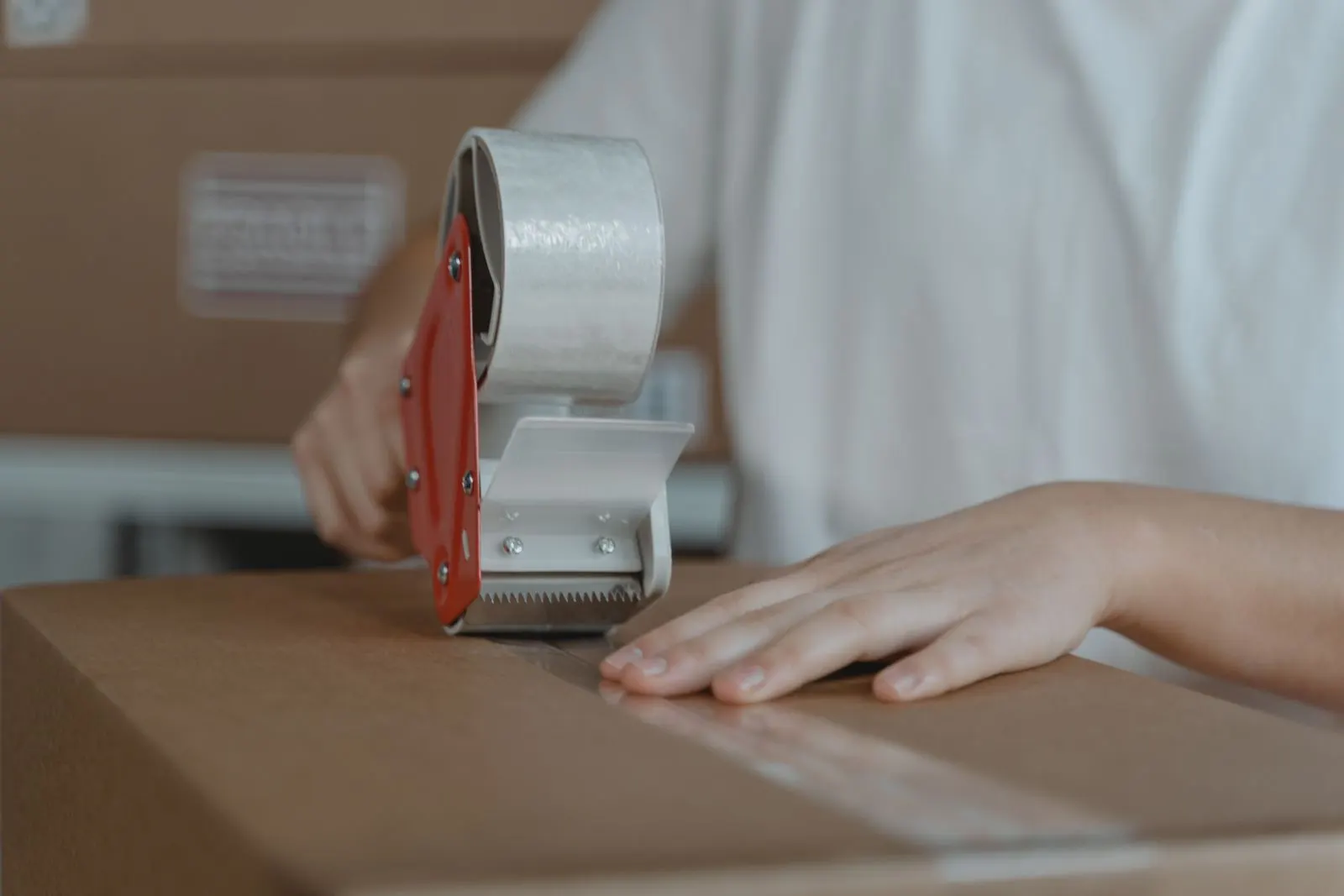 A person sealing a cardboard shipping box with a tape gun