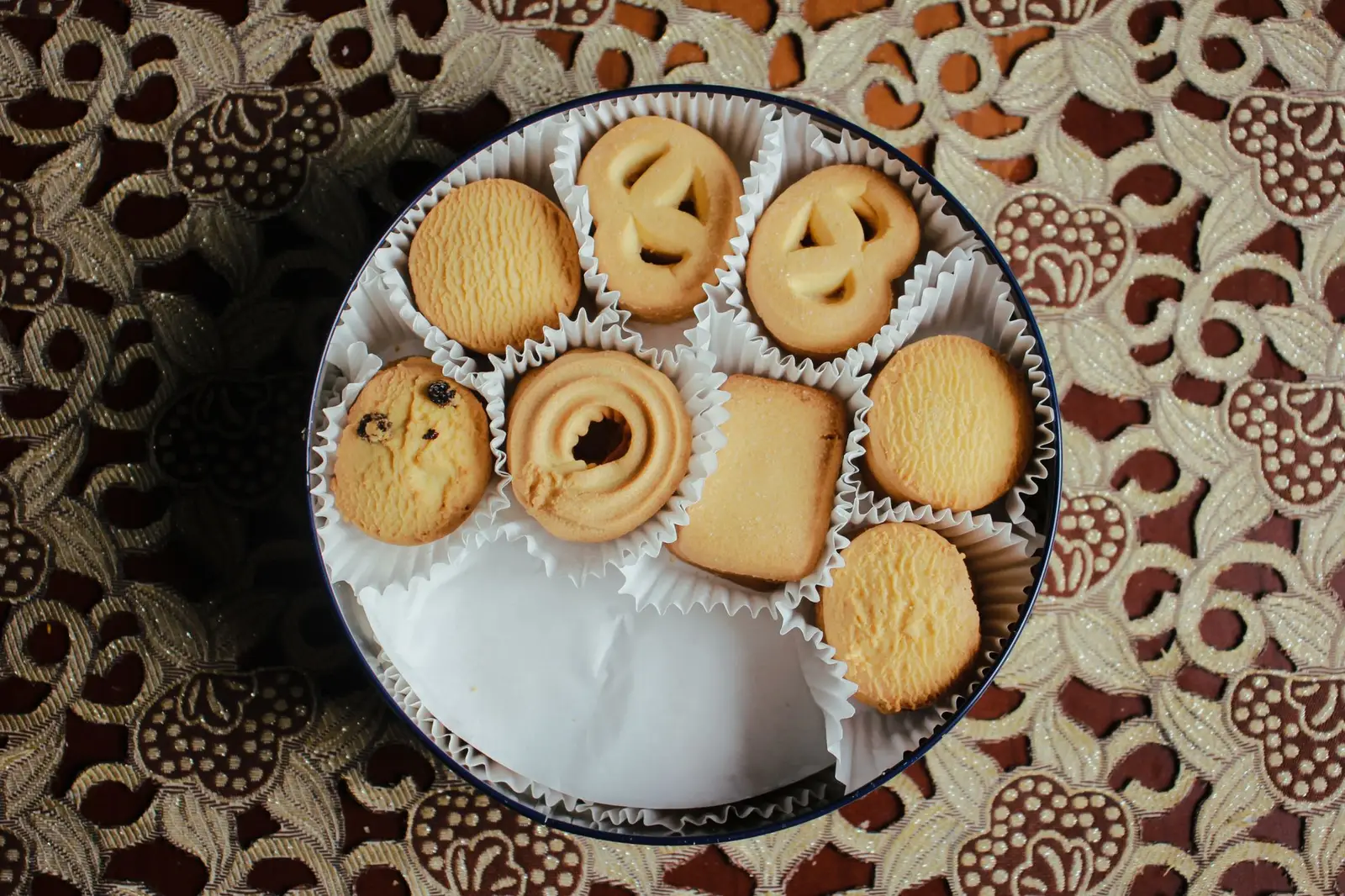 Butter cookies in a round tin on a patterned tablecloth