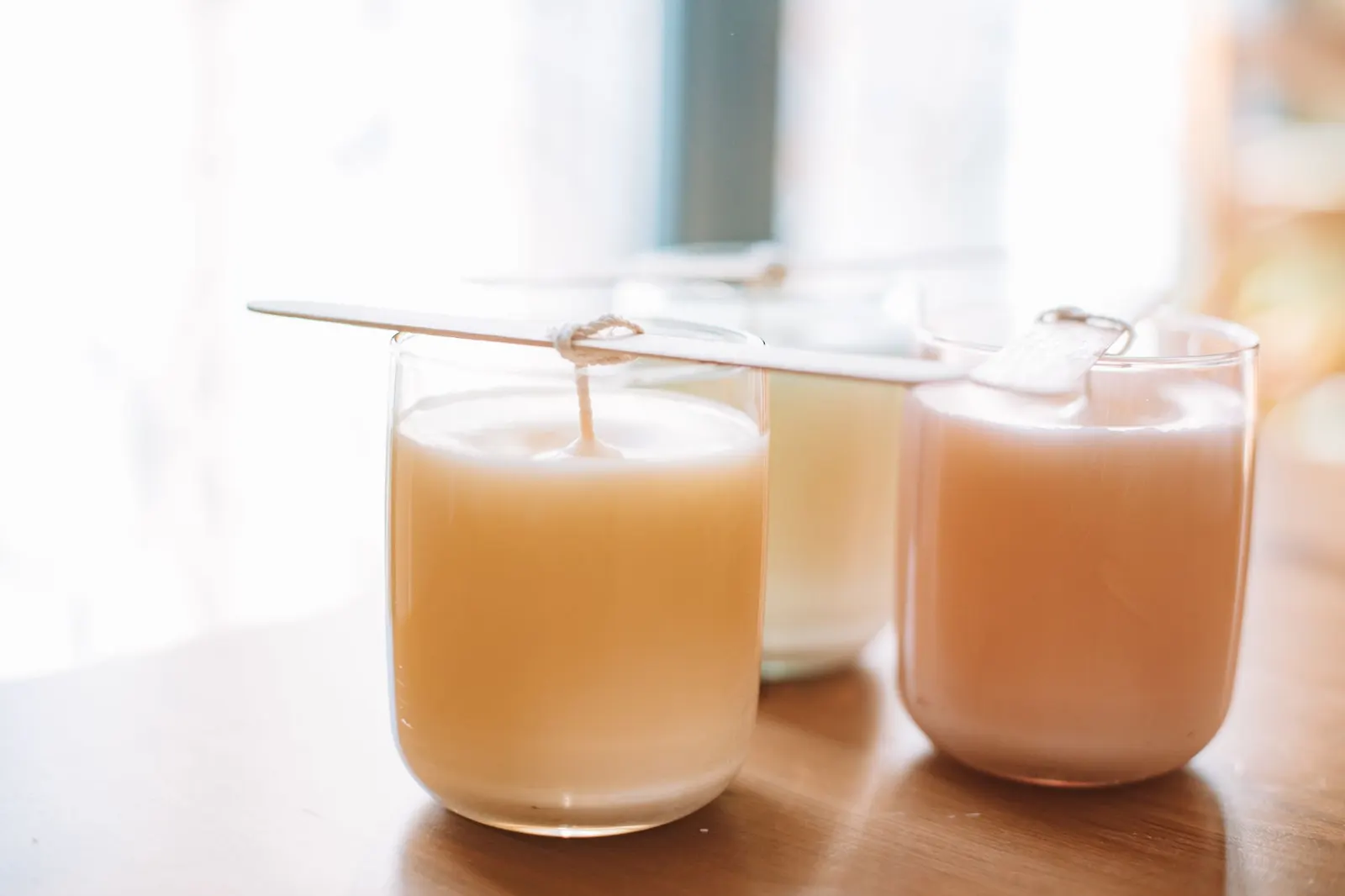 Handmade candles with wicks in clear glass jars in warm light